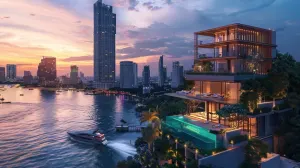 A luxurious building by a river with lights on during twilight, city skyline in the distance.