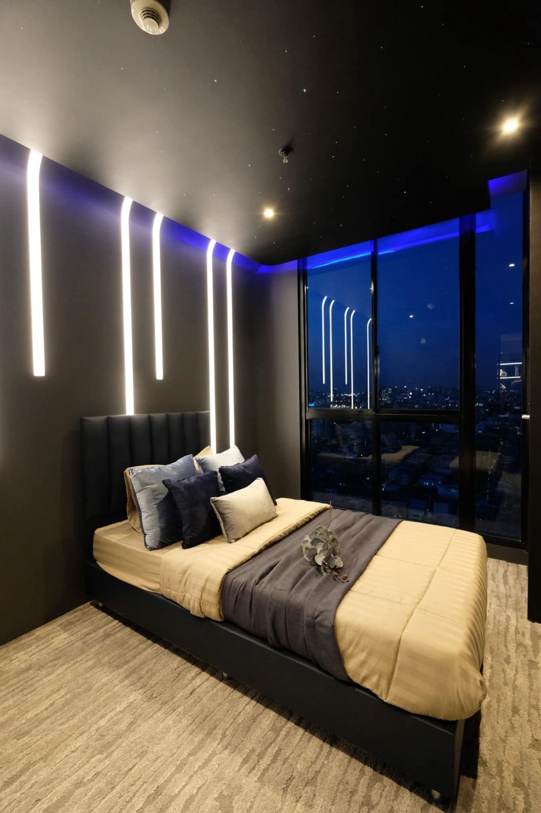 Modern bedroom with ambient lighting, city view, and cozy bedding.