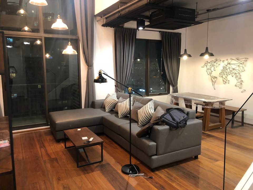 Spacious loft-style 1-bedroom duplex at Villa Asoke with high ceilings, floor-to-ceiling windows, modern furnishings, and city skyline views in Bangkok.