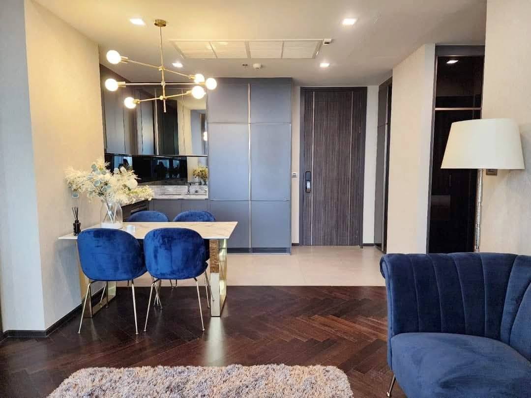 Spacious and modern living room with city views in a 2-bedroom condo at The Monument Sanampao, Bangkok, featuring elegant décor and floor-to-ceiling windows.