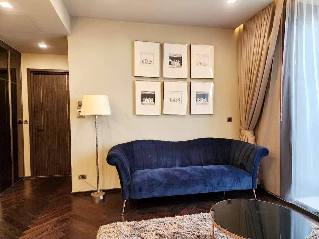 Spacious and modern living room with city views in a 2-bedroom condo at The Monument Sanampao, Bangkok, featuring elegant décor and floor-to-ceiling windows.