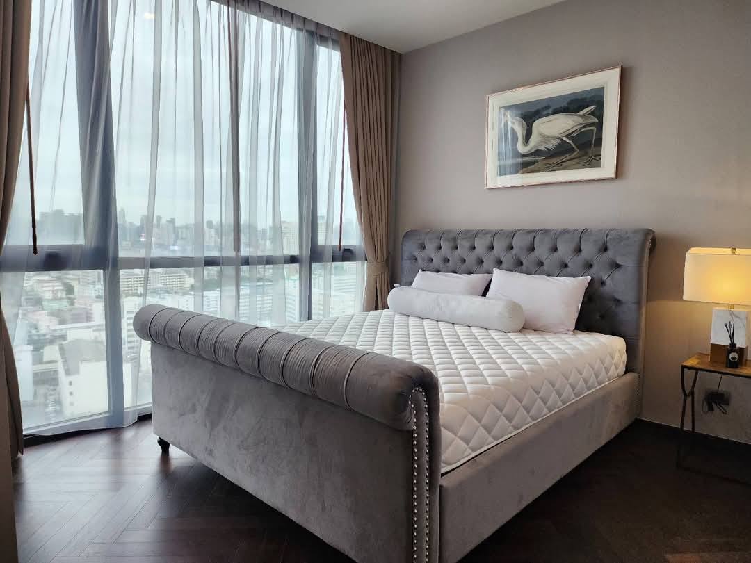 Spacious and modern living room with city views in a 2-bedroom condo at The Monument Sanampao, Bangkok, featuring elegant décor and floor-to-ceiling windows.