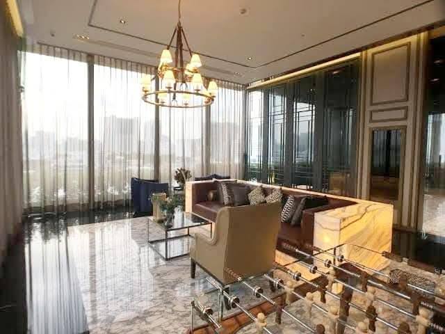 Spacious and modern living room with city views in a 2-bedroom condo at The Monument Sanampao, Bangkok, featuring elegant décor and floor-to-ceiling windows.