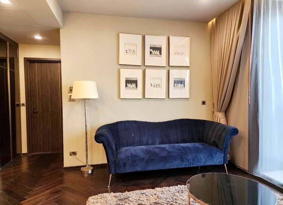 Spacious and modern living room with city views in a 2-bedroom condo at The Monument Sanampao, Bangkok, featuring elegant décor and floor-to-ceiling windows.