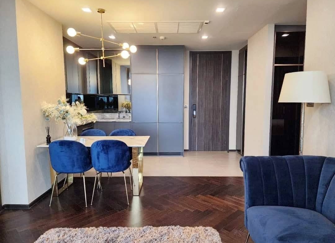 Spacious and modern living room with city views in a 2-bedroom condo at The Monument Sanampao, Bangkok, featuring elegant décor and floor-to-ceiling windows.