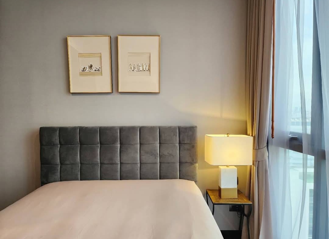 Spacious and modern living room with city views in a 2-bedroom condo at The Monument Sanampao, Bangkok, featuring elegant décor and floor-to-ceiling windows.