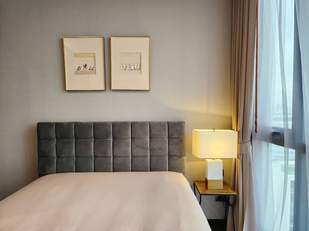 Spacious and modern living room with city views in a 2-bedroom condo at The Monument Sanampao, Bangkok, featuring elegant décor and floor-to-ceiling windows.