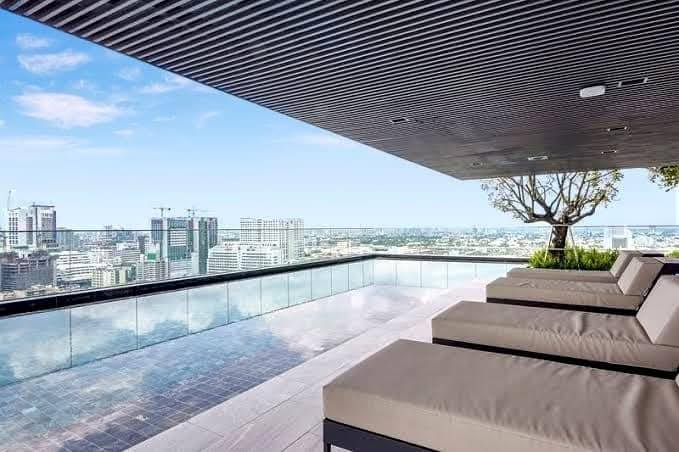 Spacious and modern living room with city views in a 2-bedroom condo at The Monument Sanampao, Bangkok, featuring elegant décor and floor-to-ceiling windows.