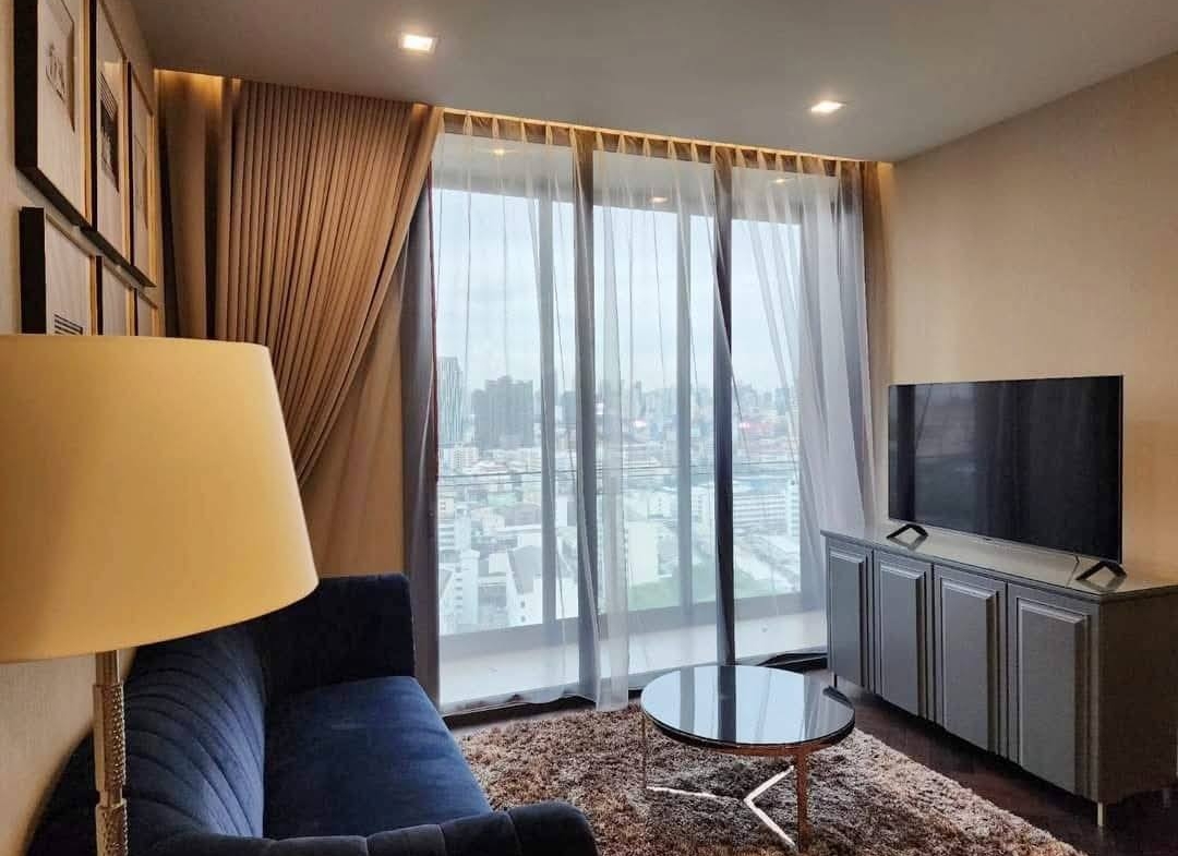 Spacious and modern living room with city views in a 2-bedroom condo at The Monument Sanampao, Bangkok, featuring elegant décor and floor-to-ceiling windows.