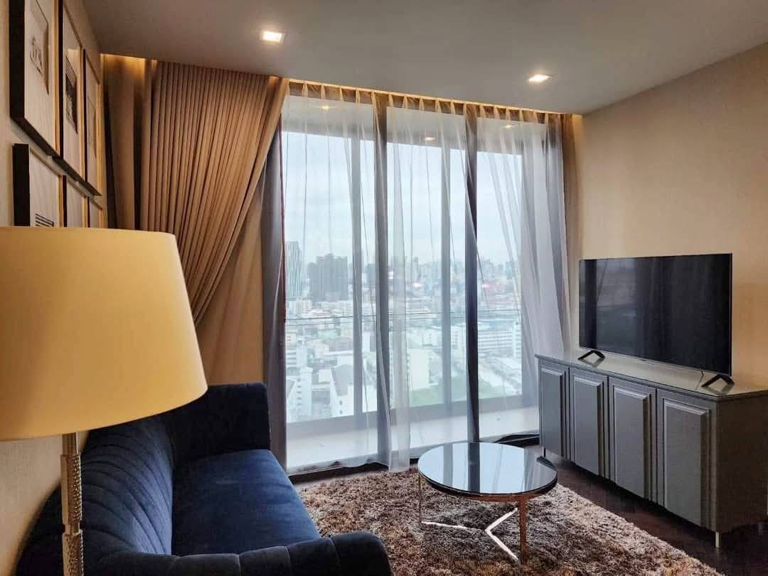 Spacious and modern living room with city views in a 2-bedroom condo at The Monument Sanampao, Bangkok, featuring elegant décor and floor-to-ceiling windows.