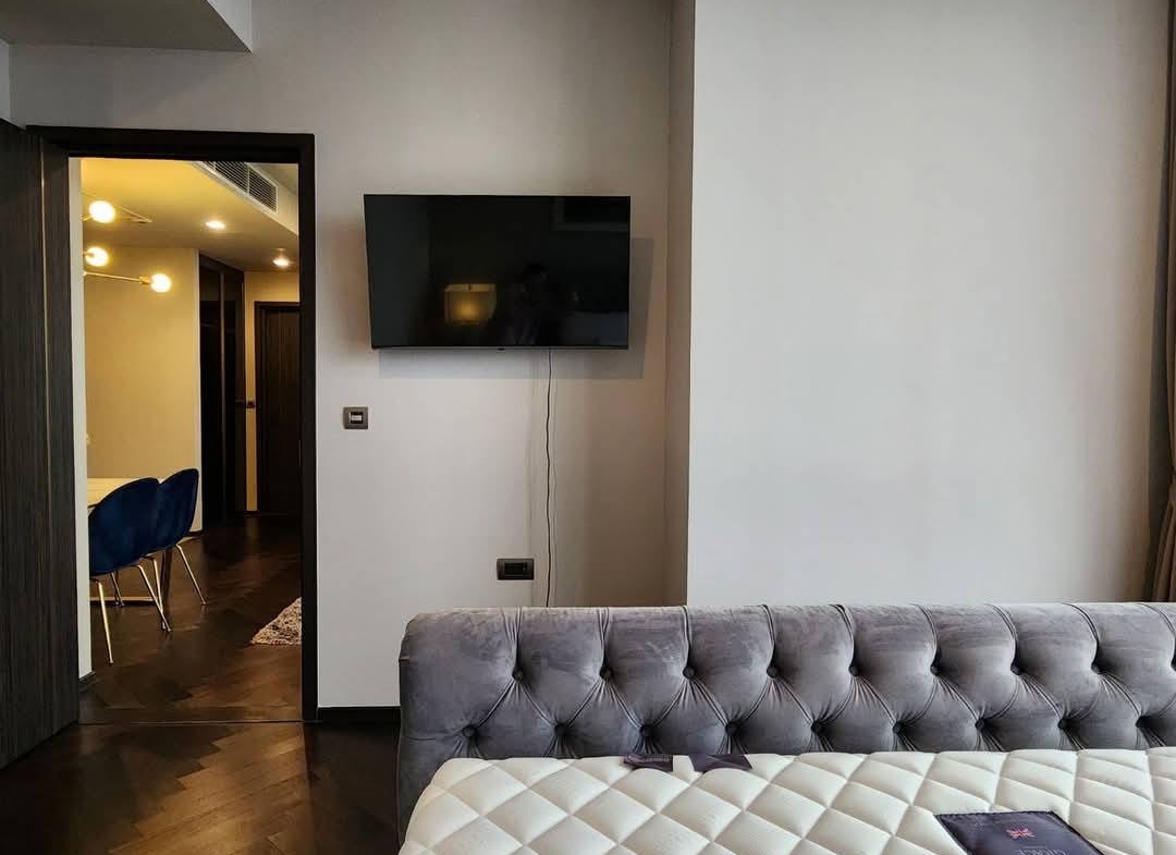 Spacious and modern living room with city views in a 2-bedroom condo at The Monument Sanampao, Bangkok, featuring elegant décor and floor-to-ceiling windows.