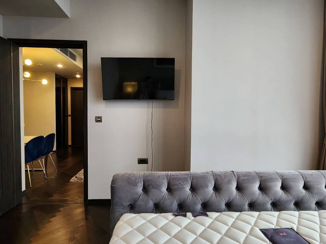 Spacious and modern living room with city views in a 2-bedroom condo at The Monument Sanampao, Bangkok, featuring elegant décor and floor-to-ceiling windows.