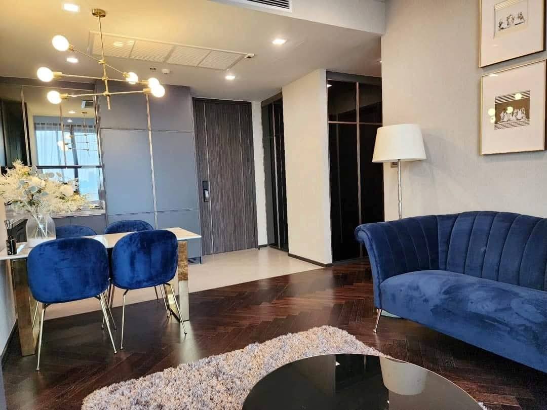 Spacious and modern living room with city views in a 2-bedroom condo at The Monument Sanampao, Bangkok, featuring elegant décor and floor-to-ceiling windows.