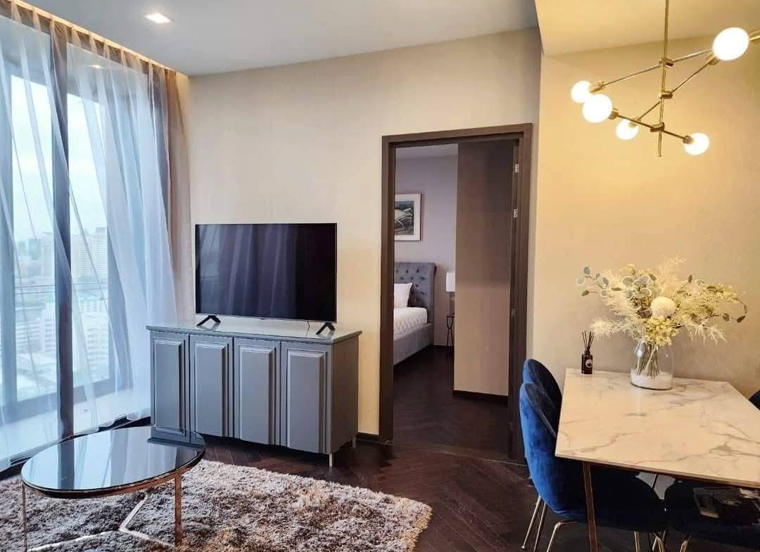 Spacious and modern living room with city views in a 2-bedroom condo at The Monument Sanampao, Bangkok, featuring elegant décor and floor-to-ceiling windows.