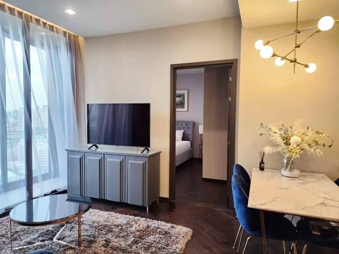 Spacious and modern living room with city views in a 2-bedroom condo at The Monument Sanampao, Bangkok, featuring elegant décor and floor-to-ceiling windows.