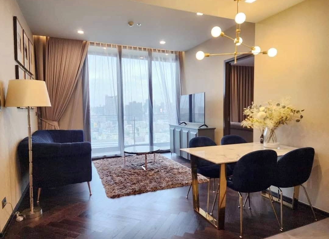 Spacious and modern living room with city views in a 2-bedroom condo at The Monument Sanampao, Bangkok, featuring elegant décor and floor-to-ceiling windows.