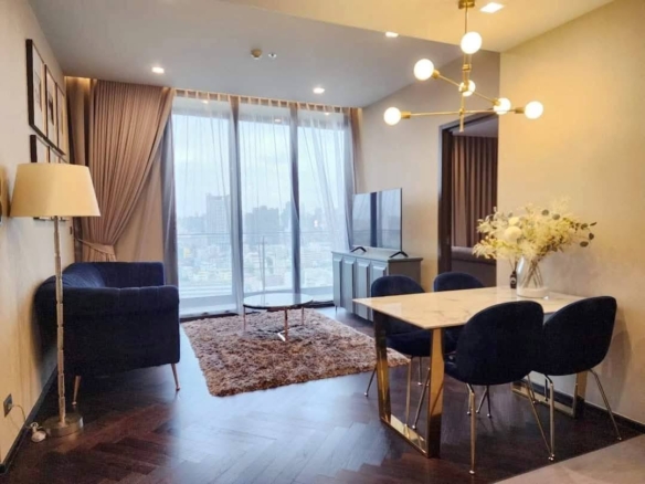 Spacious and modern living room with city views in a 2-bedroom condo at The Monument Sanampao, Bangkok, featuring elegant décor and floor-to-ceiling windows.