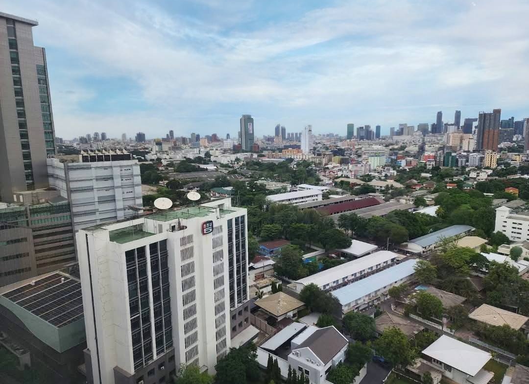 Spacious and modern living room with city views in a 2-bedroom condo at The Monument Sanampao, Bangkok, featuring elegant décor and floor-to-ceiling windows.