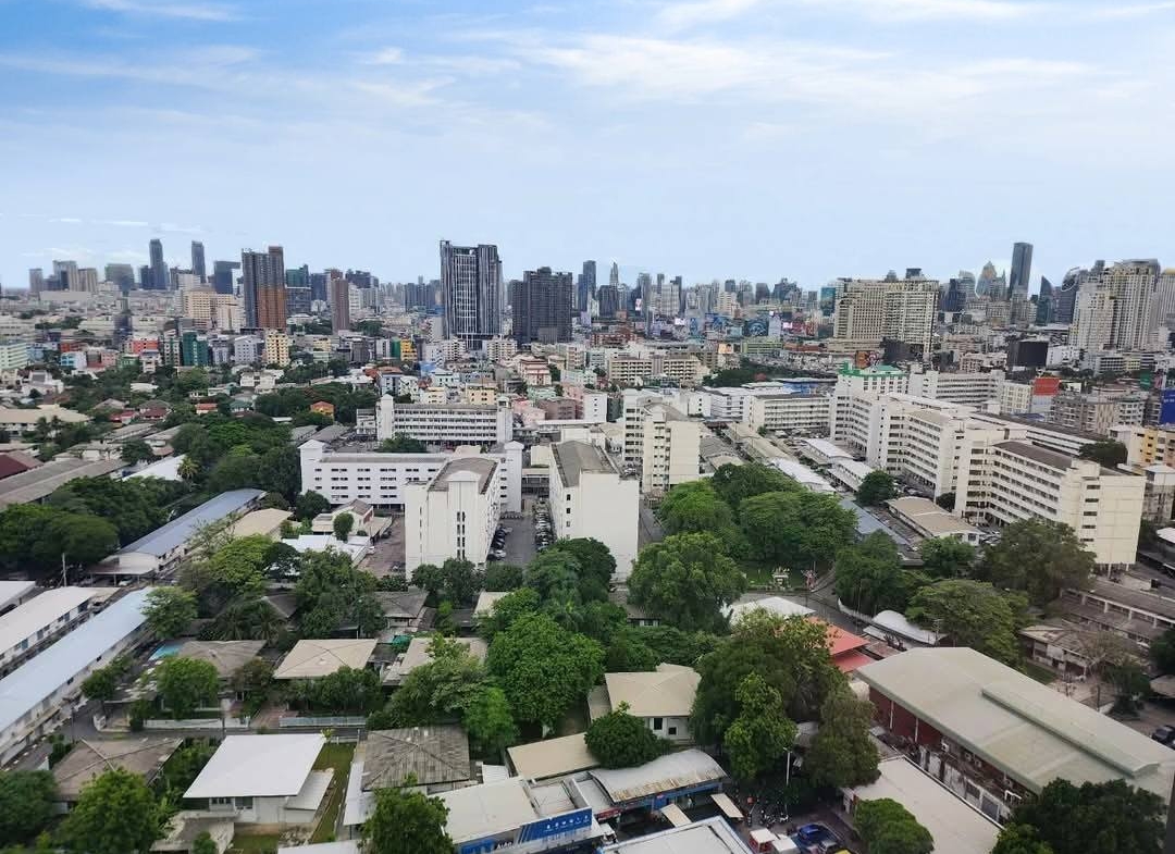 Spacious and modern living room with city views in a 2-bedroom condo at The Monument Sanampao, Bangkok, featuring elegant décor and floor-to-ceiling windows.
