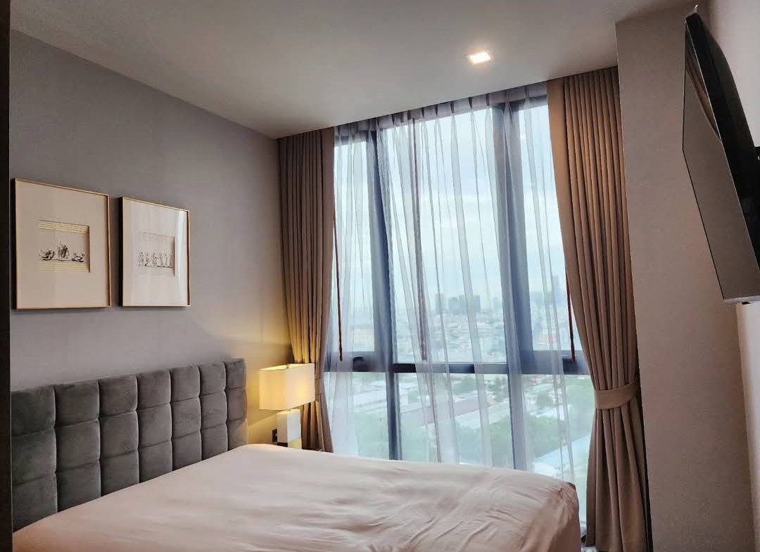 Spacious and modern living room with city views in a 2-bedroom condo at The Monument Sanampao, Bangkok, featuring elegant décor and floor-to-ceiling windows.
