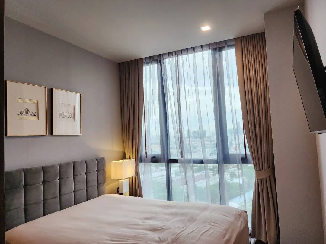 Spacious and modern living room with city views in a 2-bedroom condo at The Monument Sanampao, Bangkok, featuring elegant décor and floor-to-ceiling windows.