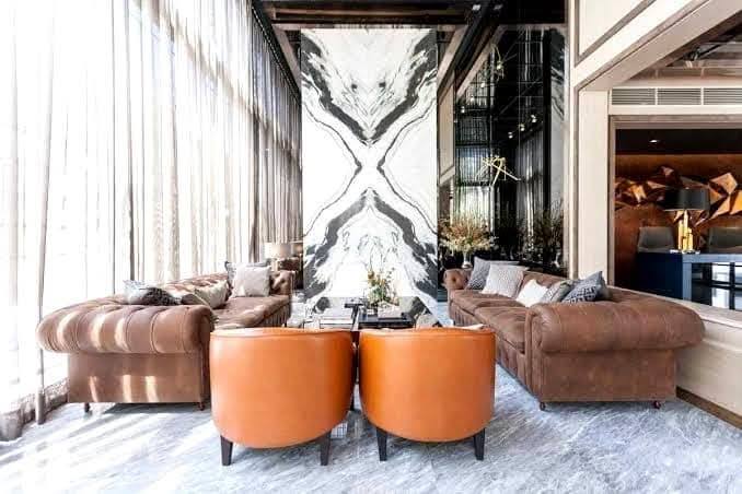 Spacious and modern living room with city views in a 2-bedroom condo at The Monument Sanampao, Bangkok, featuring elegant décor and floor-to-ceiling windows.